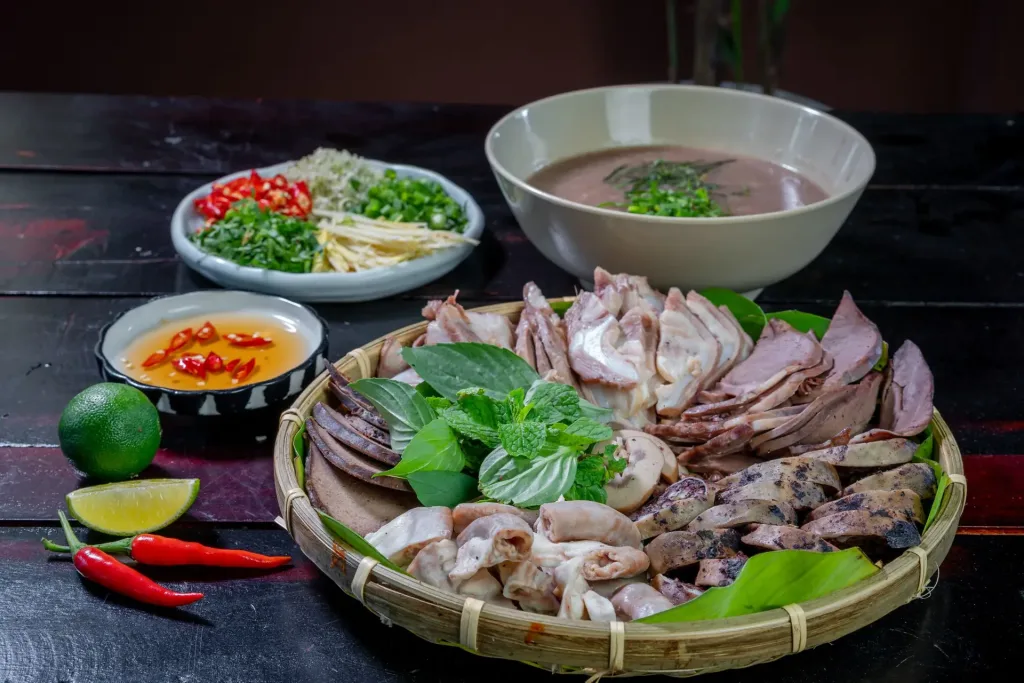 Mâm thịt luộc, rau thơm và nước chấm trên bàn gỗ tối